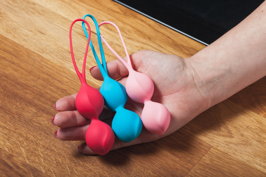 Main de femme tenant des sextoys. Boules de Kegel colorées, boules de Geisha sur fond bois. Boules vaginales multicolores dans une main de femme.